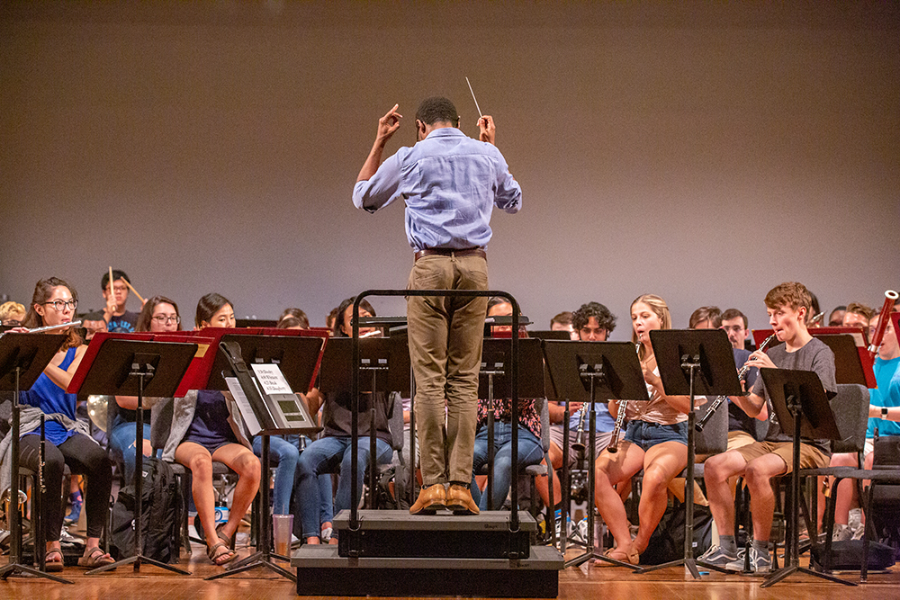 A student conductor stands on the podium-we see the conductor's back and the wind ensemble in front of them