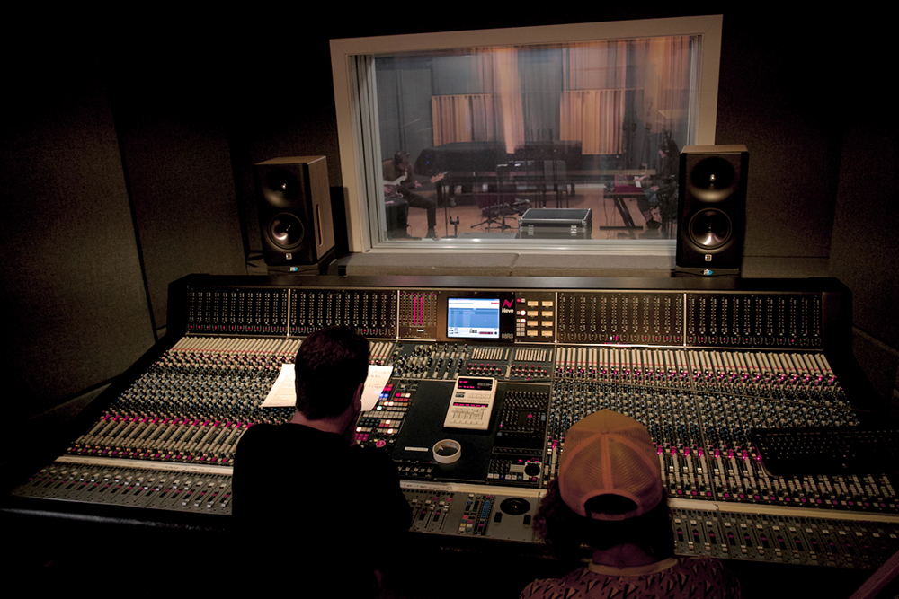A soundboard in front of a window looking into a recording studio
